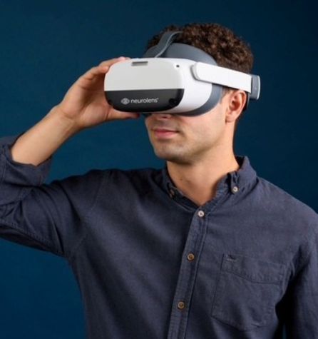 A man wearing a dark button-up shirt uses a white and gray Neurolens virtual reality headset for myopia control against a plain blue background.