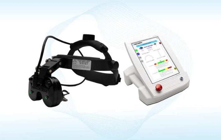 The MacuMira base unit with a black head-mounted headset featuring lenses and wires, next to a white touchscreen control unit displaying colorful data and buttons.