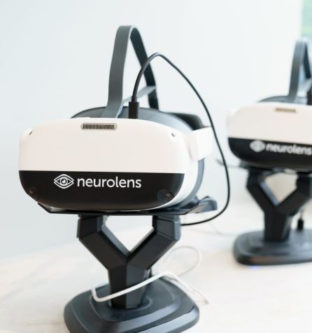 A close-up of a neurolens virtual reality headset on a stand, with another neurolens headset softly blurred in the background, set in a bright, modern environment.